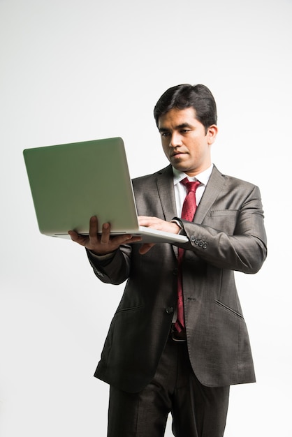 Indian Asian young businessman working on laptop computer while standing isolated over white background