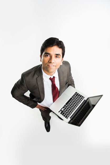 Индийский азиатский молодой бизнесмен, работающий на портативном компьютере, стоя изолированным на белом фоне