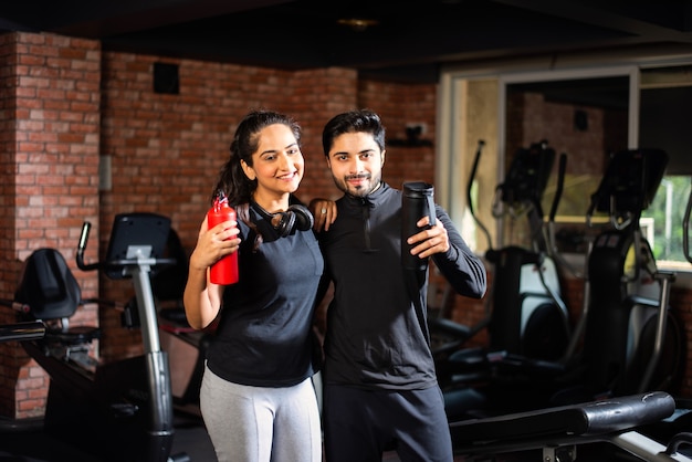 Indian asian Young couple is working out in the gym. Attractive woman and handsome fit man are training in modern gym - health and fitness concept