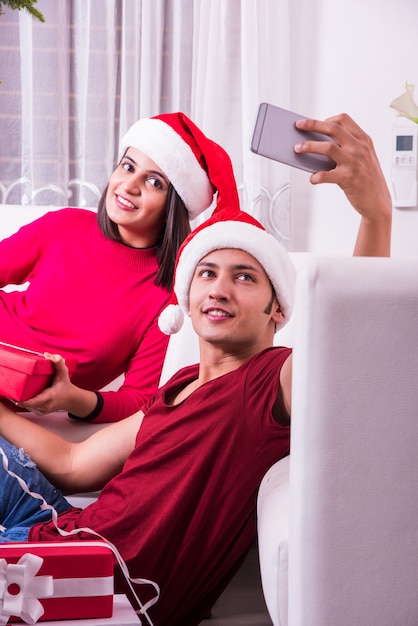Indian Asian young family celebrating Christmas with gift while wearing Santa Hat 