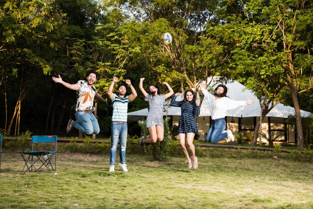 Photo indian asian young friends dancing or jumping while camping near tent, outdoors in jungle