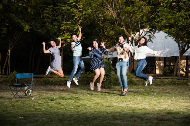 Indian asian young friends dancing or jumping while camping near tent, outdoors in jungle