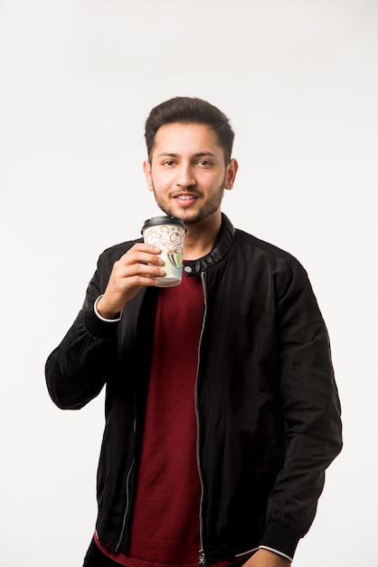 Indian asian young man holding paper coffee cup with a black plastic cap isolated on a white background in the studio, advertising coffee