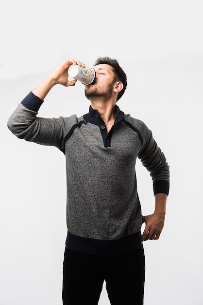 Indian asian young man holding paper coffee cup with a black plastic cap isolated on a white background in the studio, advertising coffee