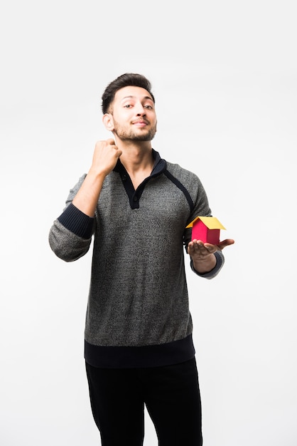 Indian asian young man with house or real estate model, standing isolated over white background