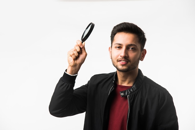 Indian asian young man with magnifying glass looking at camera or sideways