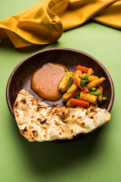 Индийское карри Baby Corn Masala, приготовленное в красном соусе, подается с роти / нааном ИЛИ индийским хлебом. На мрачном фоне. выборочный фокус