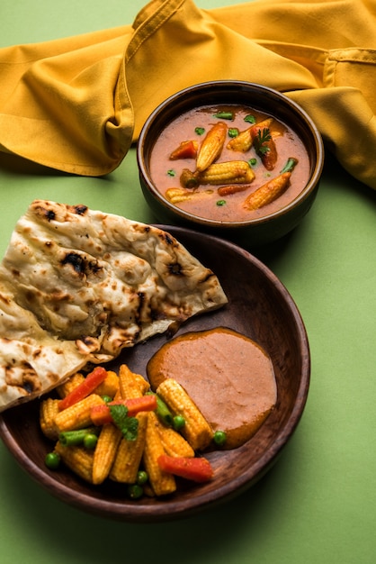 Indian Baby Corn Masala curry prepared in Red Sauce served with roti/ naan OR indian bread. Over moody background. selective focus