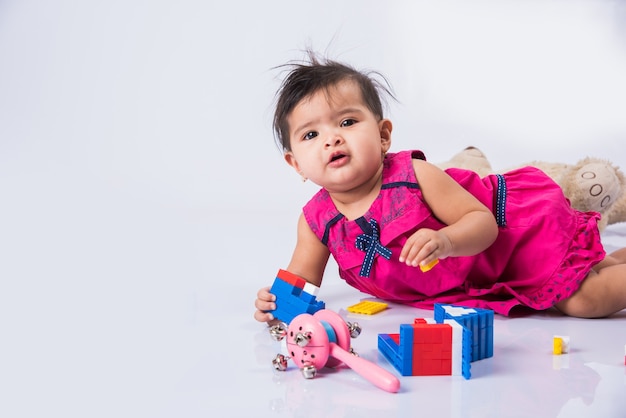 Bambino indiano che gioca con giocattoli o blocchi, bambino asiatico che gioca con i giocattoli su sfondo bianco, bambina indiana che gioca con i giocattoli, bambino indiano che gioca con i giocattoli mentre giace sul pavimento