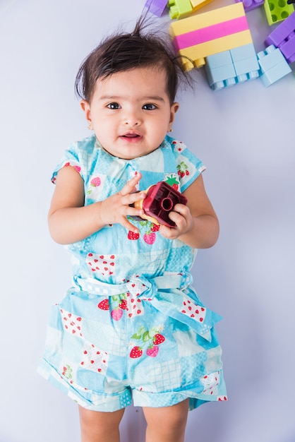 Indian baby playing with toys or blocks, asian infant playing with toys on white background, indian baby girl playing with toys, indian toddler playing with toys while lying on floor