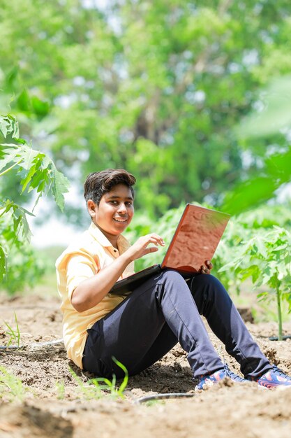 Indian boy studying in farm holding laptop in hand poor indian kids