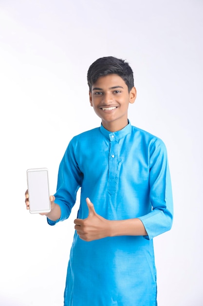 Индийский мальчик в традиционной одежде показывает смартфон на белом фоне