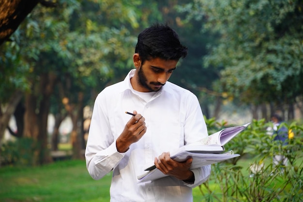 本のペンと大学のキャンパスの近くに立っているインドの少年