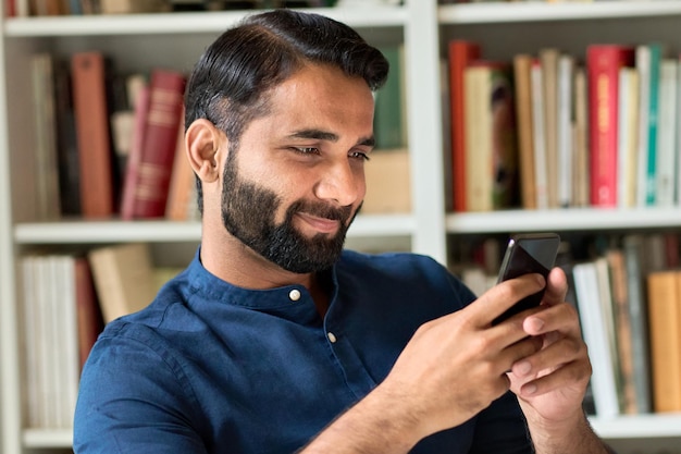 Indian business man holding smartphone using mobile phone at\
home or in office