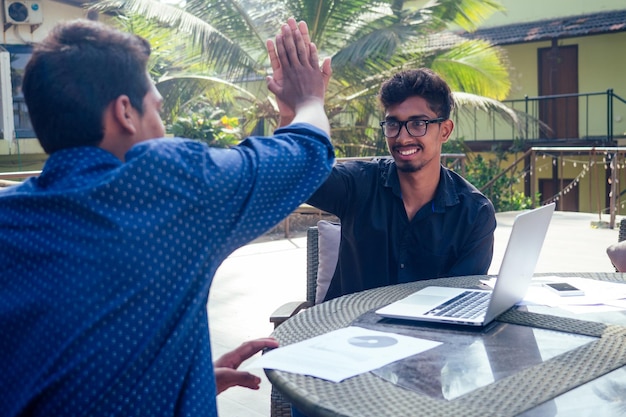 Indian businessman coach leader with multiracial business partner speaker man interview talking about a new project in summer lobby balcony outdoors cafe new delhi