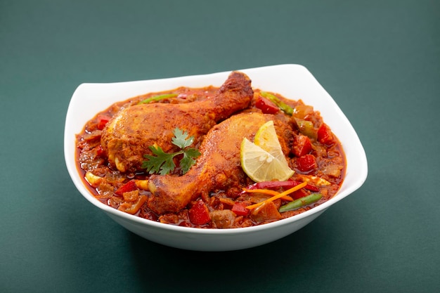 Indian Chicken curry or chicken masala ,Indian spicy chicken thick gravy  garnished with coriander leaf ,lemon slices and arranged in a white ceramic table ware or serving bowl on green background ,is