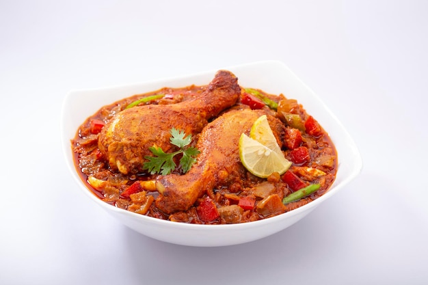 Indian Chicken curry or chicken masala ,Indian spicy chicken thick gravy  garnished with coriander leaf ,lemon slices and arranged in a white ceramic table ware or serving bowl on white background ,is