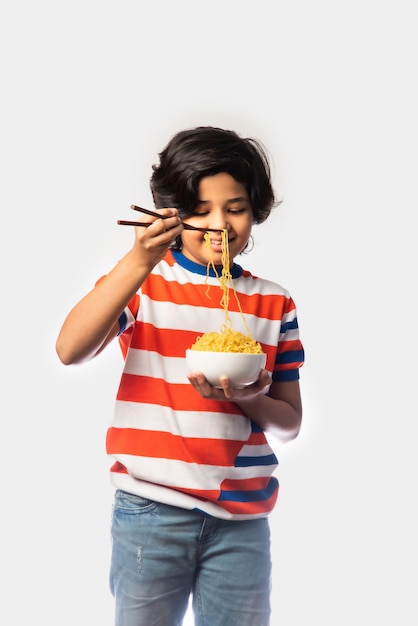 흰색 배경에 대해 포크로 맛있는 국수를 먹는 인도 아이, 아시아 소년 흰색 배경에 대해 그릇에 스파게티를 먹는다