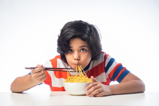 흰색 배경에 대해 포크로 맛있는 국수를 먹는 인도 아이, 아시아 소년 흰색 배경에 대해 그릇에 스파게티를 먹는다