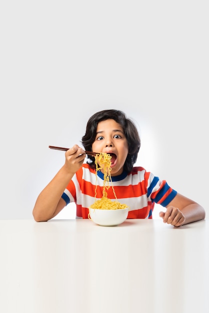 Photo indian child eating delicious noodles with fork against white background,ãâ  asian boy eats spaghetti in a bowl against white background