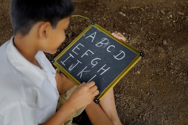 Indian child writing A B C D alphabet on Chalkboard