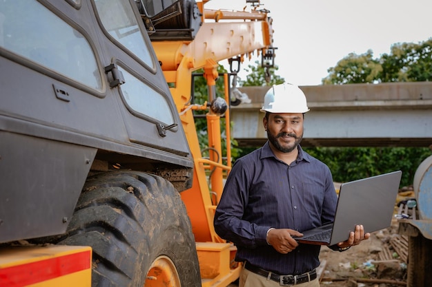 Indian civil engineer working in building construction site\
with crane construction