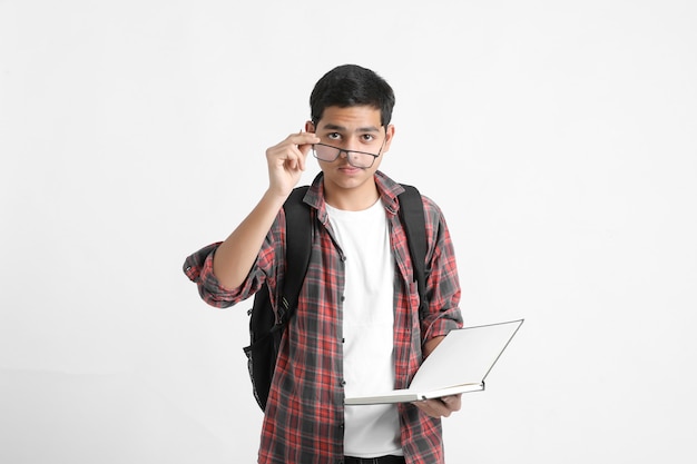 Indian college student holding books in hand and standing on white wall