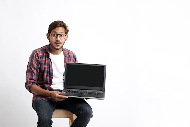 Indian college student showing laptop screen on white wall