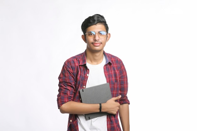 Indian college student standing with bag and reading dairy over white background.