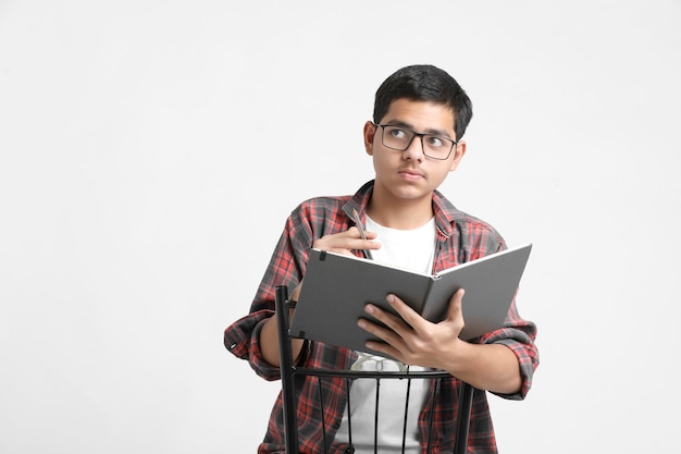 Indian college student writing some notes in notebook on white wall