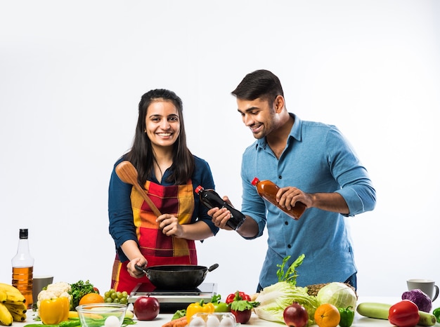 Indian couple in kitchen - Young Beautiful asian wife enjoying cooking with husband with lots of fresh vegetables and fruits