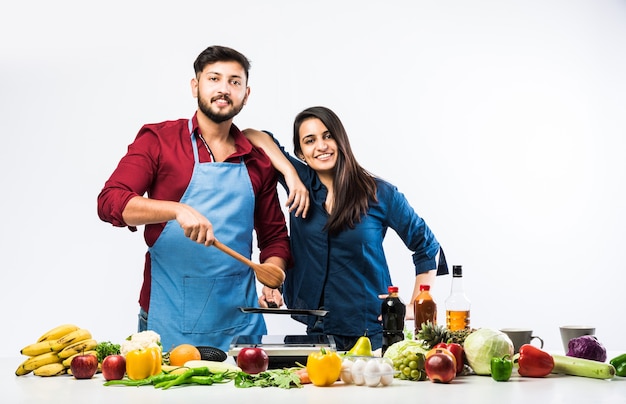 Indian couple in kitchen - Young Beautiful asian wife enjoying cooking with husband with lots of fresh vegetables and fruits