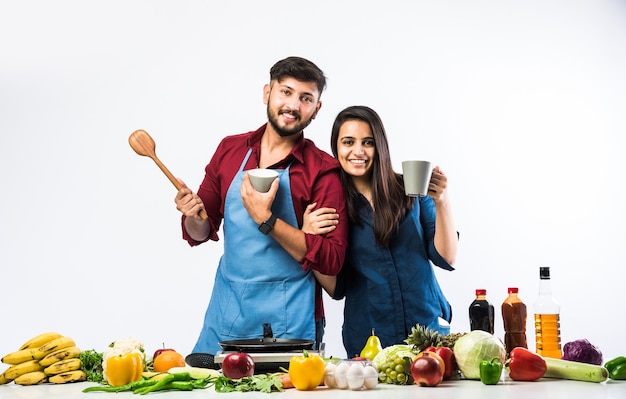 Indian couple in kitchen - Young Beautiful asian wife enjoying cooking with husband with lots of fresh vegetables and fruits