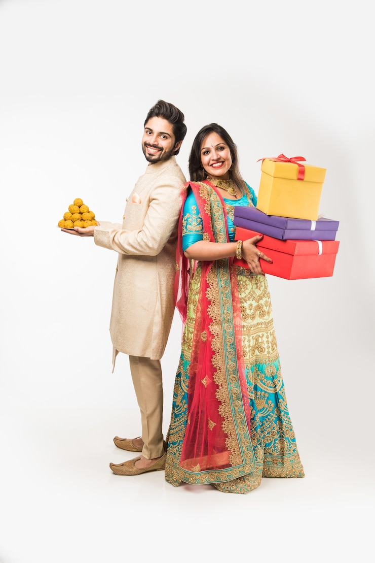 फोटो indian couple with laddu and gift boxes on diwali or festival, standing isolated over white background. wearing traditional cloths