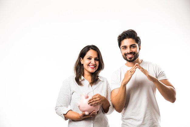 Indian couple with piggy bank standing isolated over white background