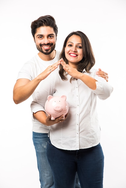 Indian couple with piggy bank standing isolated over white background