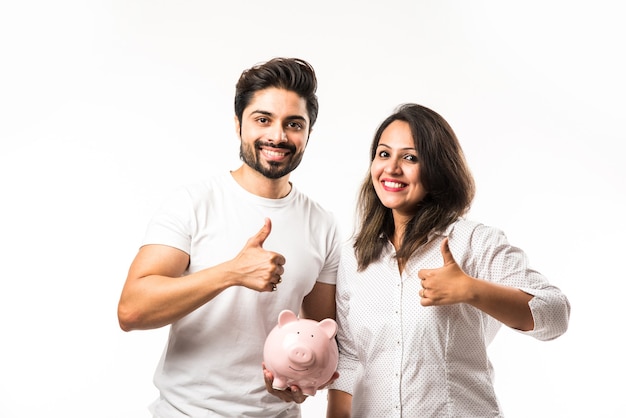 Indian couple with piggy bank standing isolated over white background