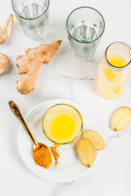 Indian cuisine recipes. Healthy food detox water. Traditional Indian refreshing drink from turmeric and ginger in glasses bottles on a white marble table.