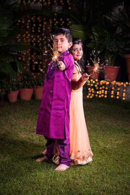 Indian cute Boy and girl in traditional wear playing with sparklers or fulzadi or phuljhadi on diwali night