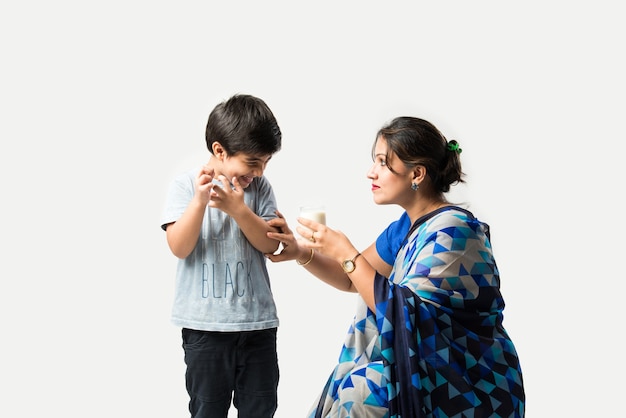 Indian cute boy making tantrums while drinking milk with mother scolding