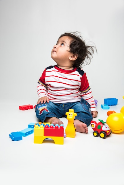 Indian cute little baby or infant or toddler playing with colourful toys or blocks over white background,