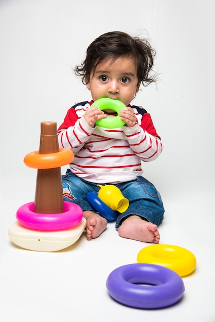 Indian cute little baby or infant or toddler playing with toys or blocks over white background,