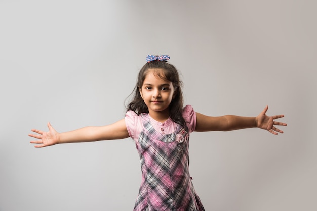 Индийская милая маленькая девочка с двумя руками, распростертыми как крылья на белом фоне.