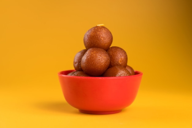 Indian dessert of sweet dish: gulab jamun in kom op gele achtergrond.