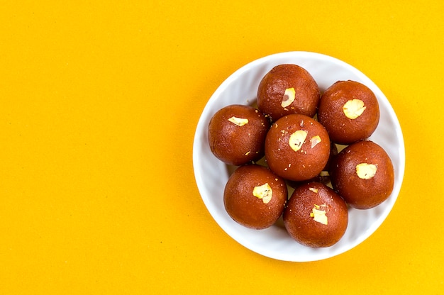 写真 インドのデザートや甘い料理：黄色の背景に白いボウルでgulab jamun