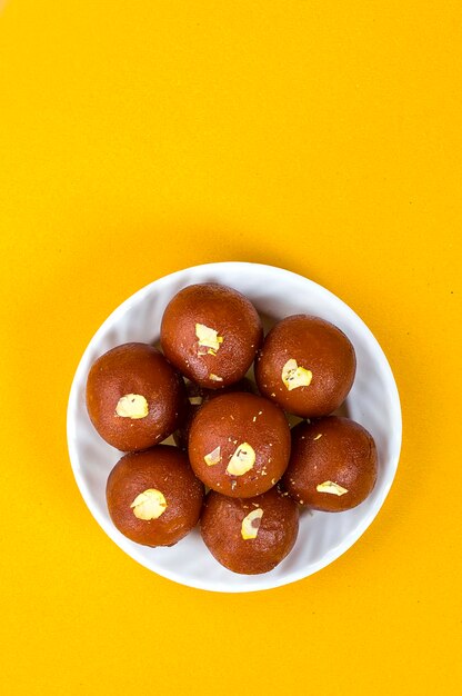 Photo indian dessert or sweet dish gulab jamun in white bowl on yellow background