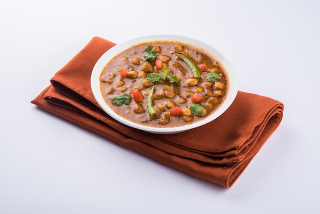 촐라(Chola) 또는 차나 마살라(Chana Masala) 또는 일반적으로 촐레(Chole)라고도 알려진 인도 요리 매운 병아리 완두콩 카레는 다채로운 또는 나무 배경 위에 튀긴 푸리 또는 푸리와 함께 제공됩니다. 선택적 초점