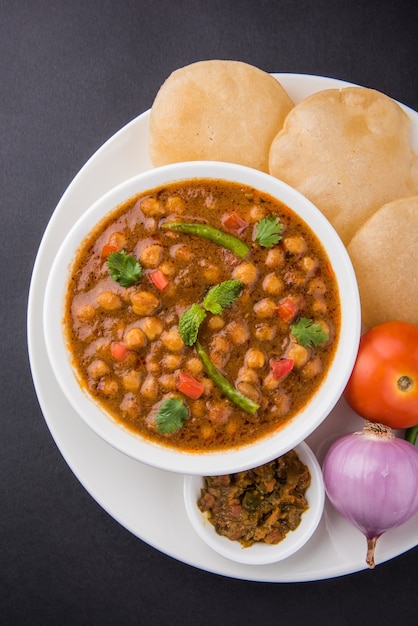 촐라(Chola) 또는 차나 마살라(Chana Masala) 또는 일반적으로 촐레(Chole)라고도 알려진 인도 요리 매운 병아리 완두콩 카레는 다채로운 또는 나무 배경 위에 튀긴 푸리 또는 푸리와 함께 제공됩니다. 선택적 초점