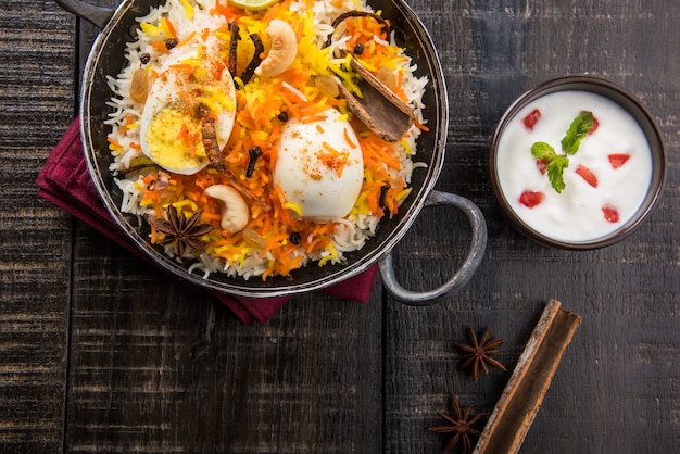 Indian Egg Biryani or anda rice served in kadhai or kadai with yogurt dip, selective focus