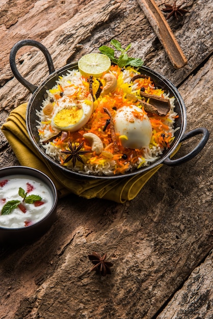 Indian Egg Biryani or anda rice served in kadhai or kadai with yogurt dip, selective focus